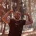 a man flexing his muscles in the woods
